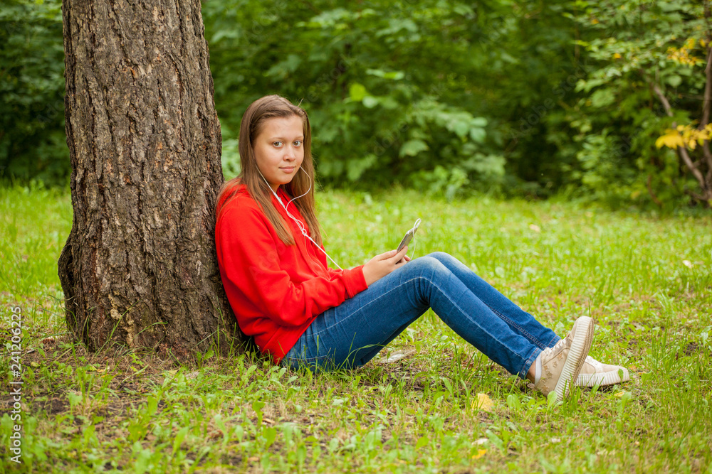 modern teenager girl sitting on the grass in the park with a smartphone in her hands modern teenager girl sitting on the grass in the park with a smartphone in her hands