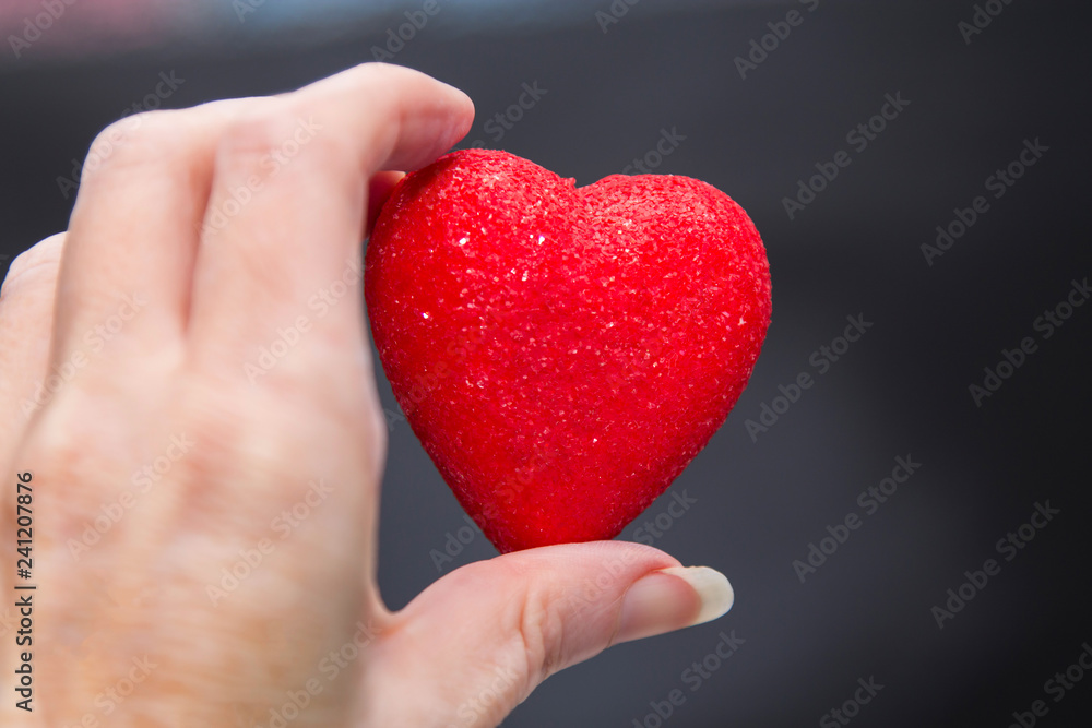 female hand holding red heart with black background