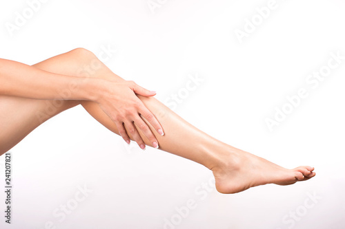 Female hand with french manicure touches barefoot leg, isolated on white