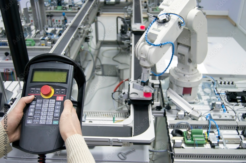 Man is holding teach panel (tablet) to control a robotic arm which is integrated on smart factory manufacturing line. industry 4.0 automation line which is equipped with sensors and robotic arm. Man is holding teach panel (tablet) to control a robotic arm which is integrated on smart factory manufacturing line. industry 4.0 automation line which is equipped with sensors and robotic arm.