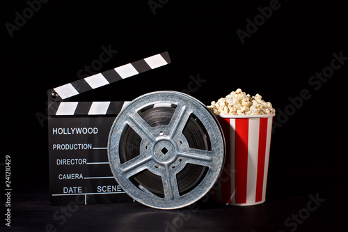 movie film reel and film clapper with popcorn box on black