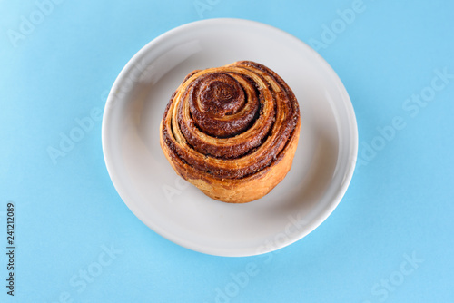 Cinnamon Danish Swirl-classic buttery danish pastry rolled with cinnamon and glazed with sugar on dish on blue paper background. Flat lay. Top view. © Inna