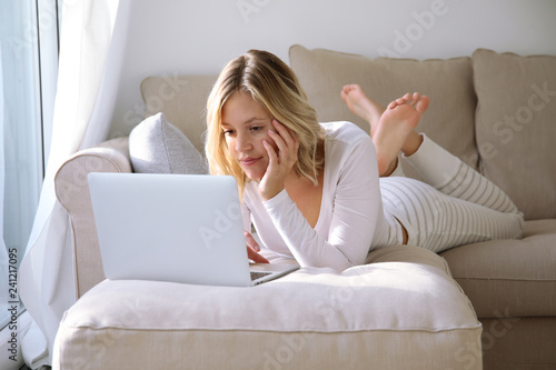 Junge Frau mit Laptop liegt auf einer Couch