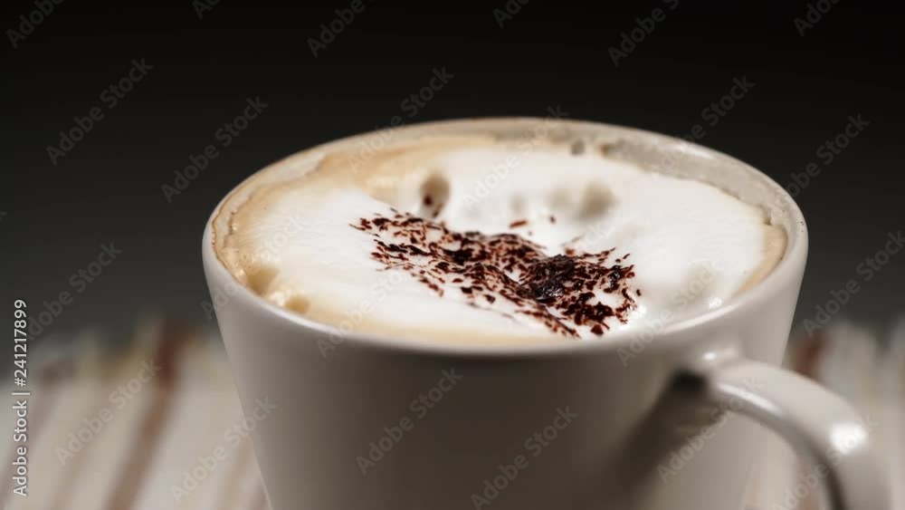 Close up hot coffee cup with milk foam and chocolate decoration rotating on black background Close up hot coffee cup with milk foam and chocolate decoration rotating on black background