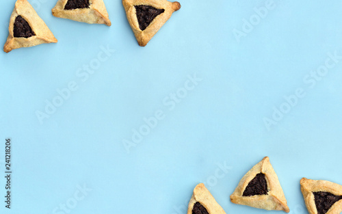 Triangular cookies with poppy seeds ( hamantasch or aman ears ) for jewish holiday of purim celebration on blue paper background with space for text. Top view, flat lay photo