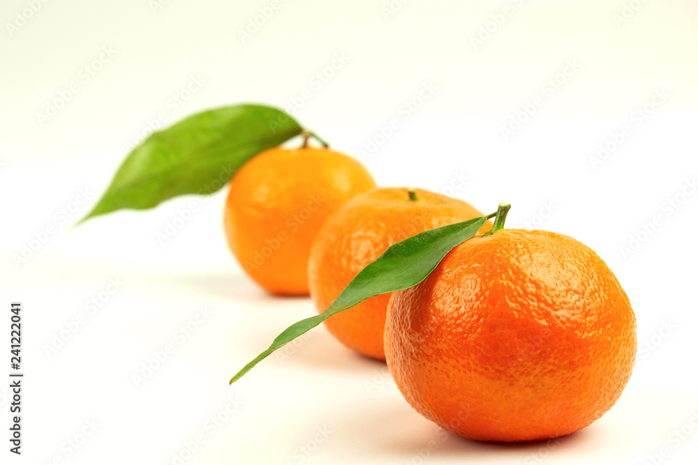Three ripe tangerines in one line with green leaves on a white background Three ripe tangerines in one line with green leaves on a white background