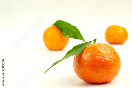 Three ripe tangerines with green leaves on a white background