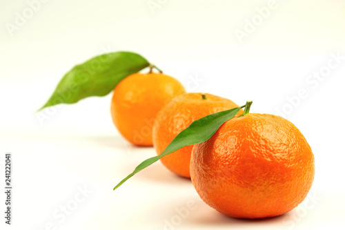 Three ripe tangerines in one line with green leaves on a white background