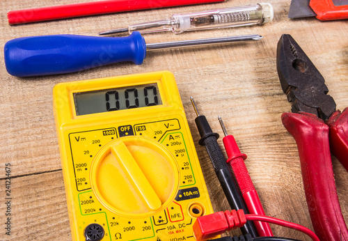 Electrical tester and other tools of electrician on a wooden background.