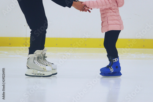 father teaching daughter to skate at ice-skating rink