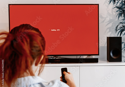 woman sitting in her living room and holding a TV remote control in front of a screen display waiting message photo