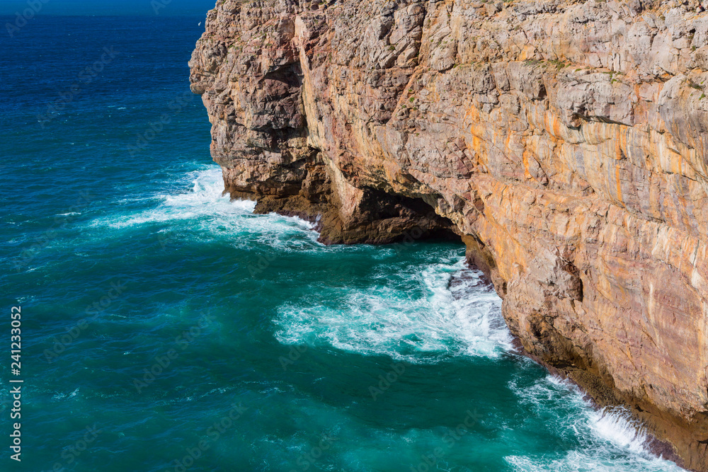 Sea waves hitting rock cliff with a cave at Fortaleza de Sagres, Portugal Sea waves hitting rock cliff with a cave at Fortaleza de Sagres, Portugal