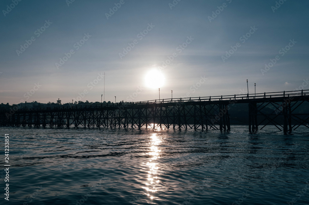 Fototapeta premium Silhouette of wooden and long bridge over the river (Mon Bridge) in the evening 