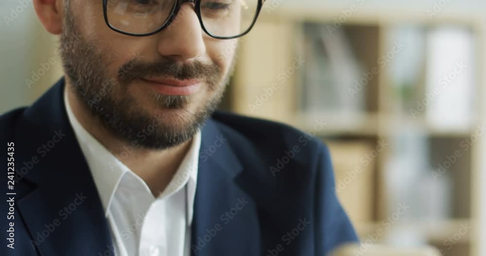 Smartphone device in hands of the young smiled attractive man while he typing as chatting on it. Close up Portrait. Inside. Smartphone device in hands of the young smiled attractive man while he typing as chatting on it. Close up Portrait. Inside.