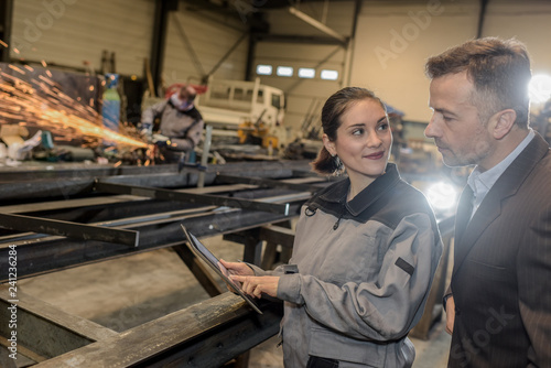 Happy female factory worker shows her tablet to her boss