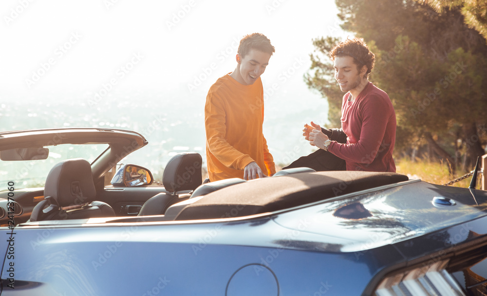 Two guys at sunrise laughing with blue car in viewpoint