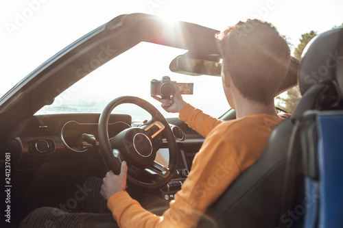 Smiling boy taping himself with camera in sportive car
