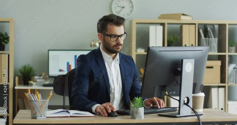 Portrait shot of the handsome official worker man typing on the keyboard of the computer in the nice cabinet room. Portrait shot of the handsome official worker man typing on the keyboard of the computer in the nice cabinet room.