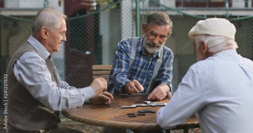 Cheerful Caucasian old men playing a domino game at the fresh air and one of them winning. Outside. Cheerful Caucasian old men playing a domino game at the fresh air and one of them winning. Outside.