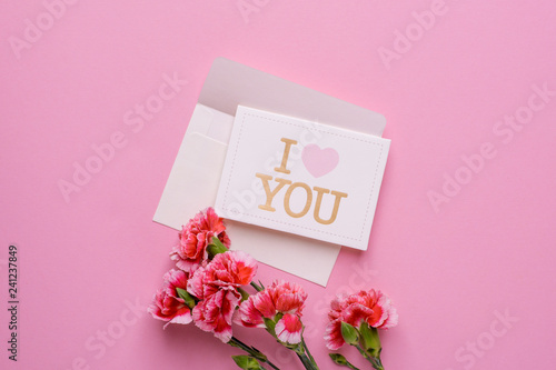 An envelope with card I love you and pink flowers on a pink background