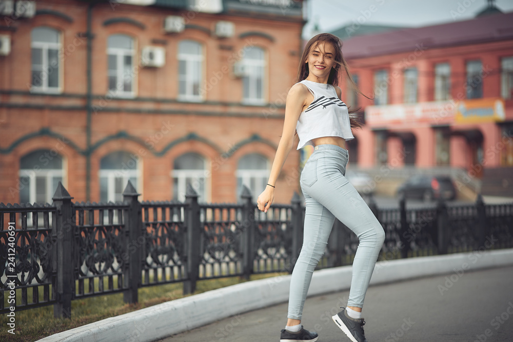 portrait of a girl in jeans and a t-shirt on the background of the building in the evening on a summer day. street dancing in the city