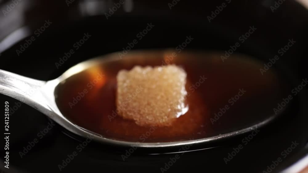Sugar cube dissolves at rapid speed in tea spoon of black coffee. 4K UHD macro