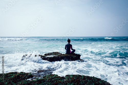 Woman meditation at the seaside croal cliff edge facing the coming sea waves photo