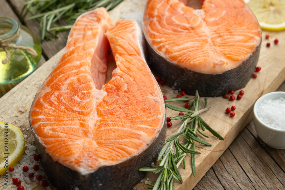 Two raw salmon fish steaks with lemon slices, salt and rosemary on cutting board. Two raw salmon fish steaks with lemon slices, salt and rosemary on cutting board.