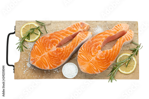 Two raw salmon fish steaks with lemon slices, salt and rosemary on cutting board. Top view, isolated on white.