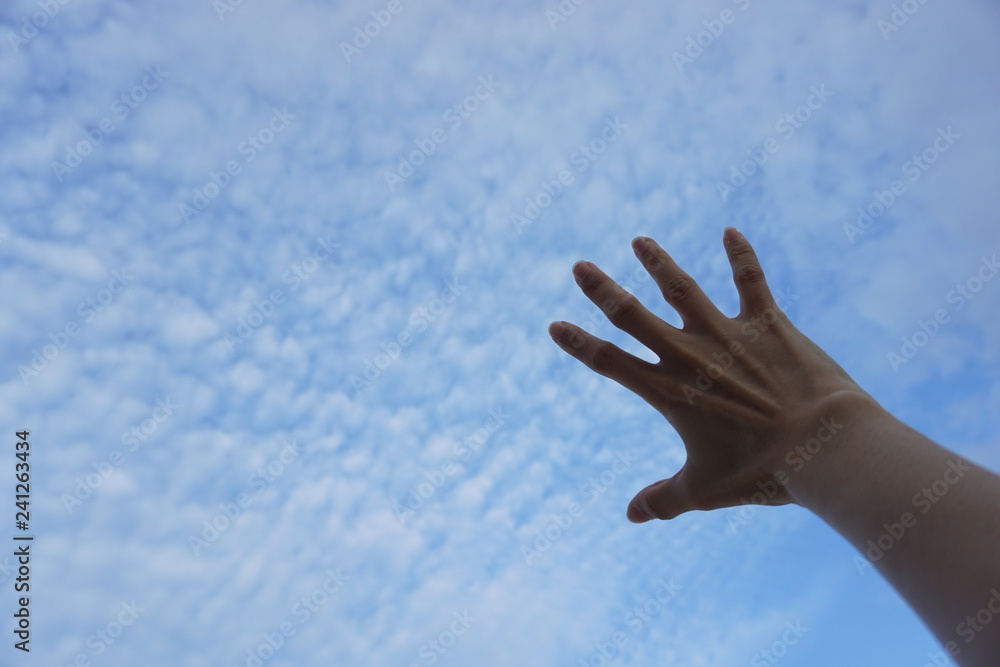 Hand reaching to towards blue sky and clouds. Hand on the sky background. Hand reaching to towards blue sky and clouds. Hand on the sky background.