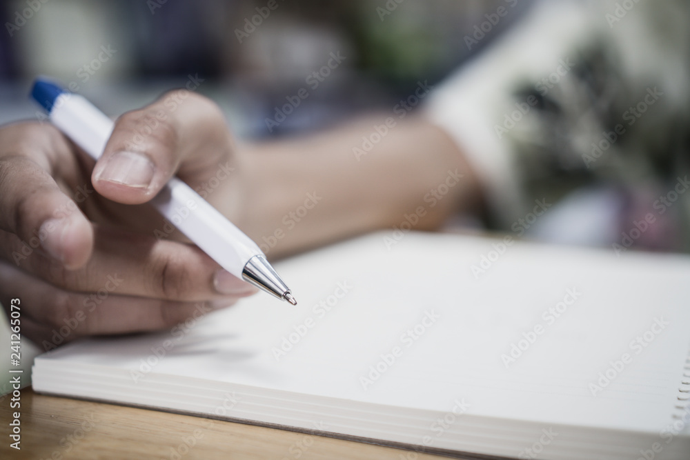 Man student taking and writing notes on notebook with pen in library at college university for homework. Education learning studying in school concept