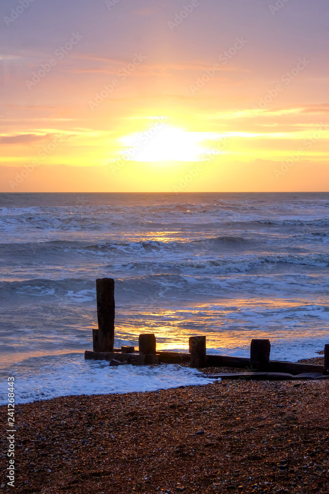 sun setting over a sea with waves breaking and a wooden sea break, Brighton, Uk