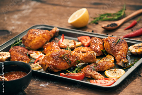Grilled chicken drumstick and wings on baking tray over wooden table