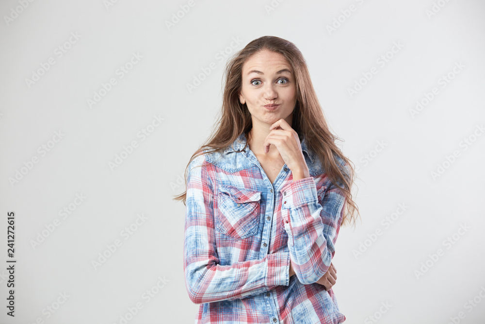 Surprised girl dressed in a checkered shirt stands on the white background in the studio Surprised girl dressed in a checkered shirt stands on the white background in the studio