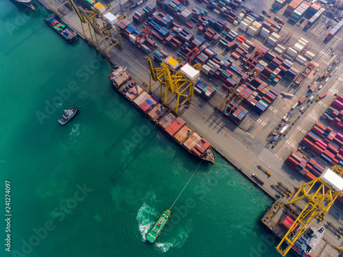Aerial top view Tug boat draging container ship at sea port to crane bridge for load container, logistics import export, shipping or transportation concept. © Pawinee