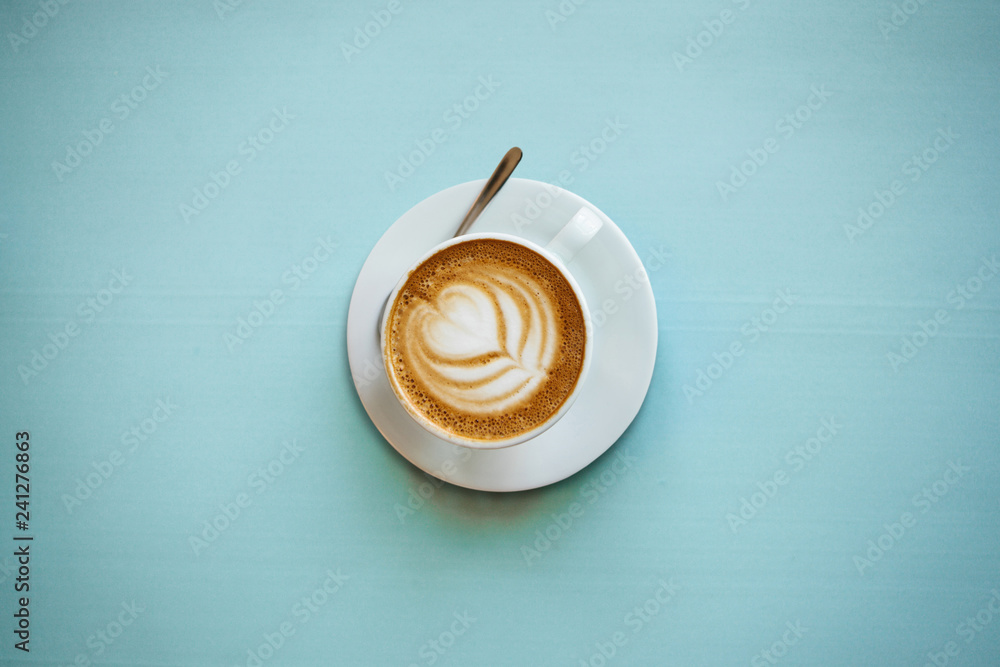 A cup with a traditional tasty and aromatic morning cappuccino on a blue background.