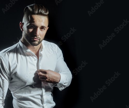 People, business, fashion and clothing concept. Close up of man in shirt dressing up at home. Businessman dressing up for work. Man buttons up his white shirt standing on black background.
