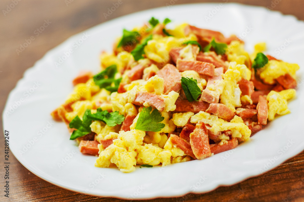 scrambled eggs with ham and cheese in white plate on wooden table background scrambled eggs with ham and cheese in white plate on wooden table background