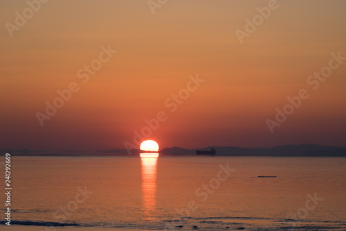 Seascape in orange and with bright sun on the horizon.