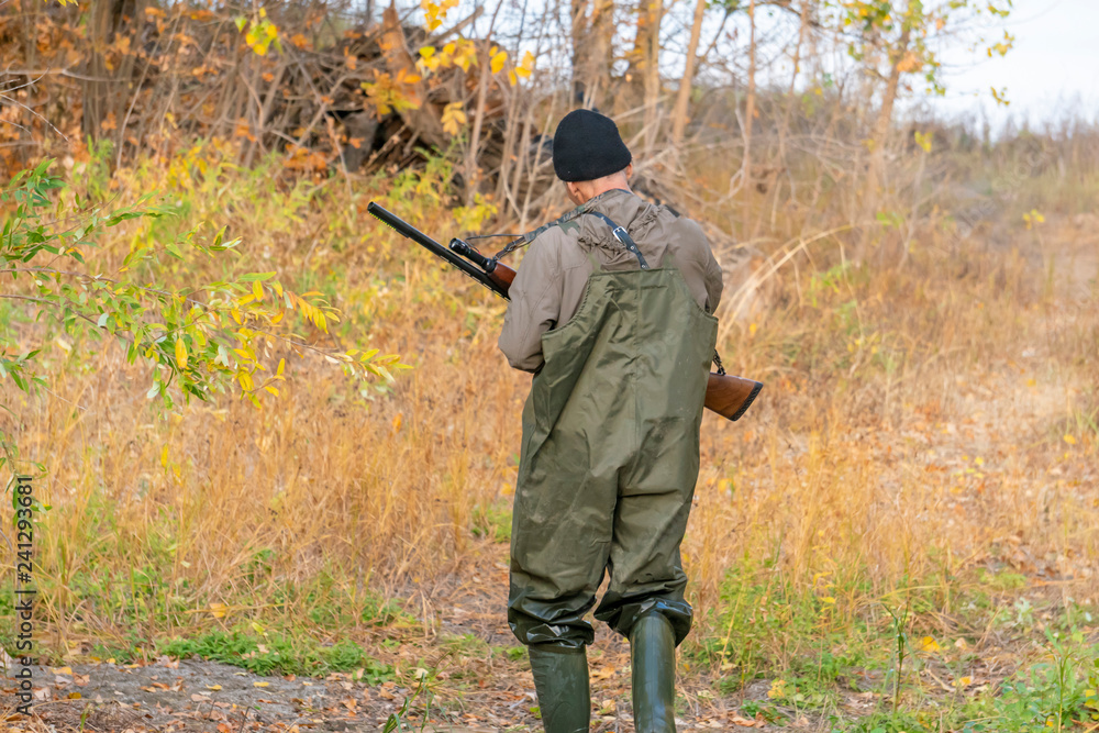 Fototapeta premium hunter with shotgun wearing waterproof uniform crossing river b