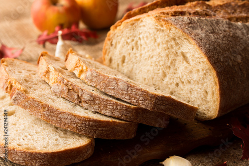   Pokorojony świeży chleb w kompozycji z jesiennymi liśćmi i czosnkiem.