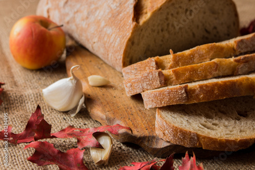   Pokorojony świeży chleb w kompozycji z jesiennymi liśćmi i czosnkiem.