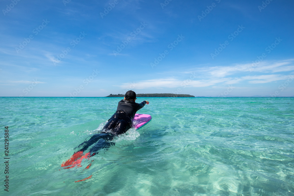 Asian kid surfing at turquoise sea on sunshine day with blue sky background Asian kid surfing at turquoise sea on sunshine day with blue sky background