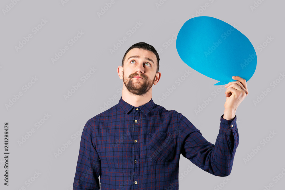 Young handsome man with facial hair holding blank paper speech bubble in hands with copy space for text. Bearded male, wearing hipster checkered shirt with empty message box. Isolated, background.