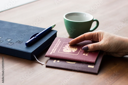 Travel, working, holiday, business concept. A woman holding a Russian passport in her hands on the background of a notebook and cup. People is planning trip or vacation. Close up of woman's hands.