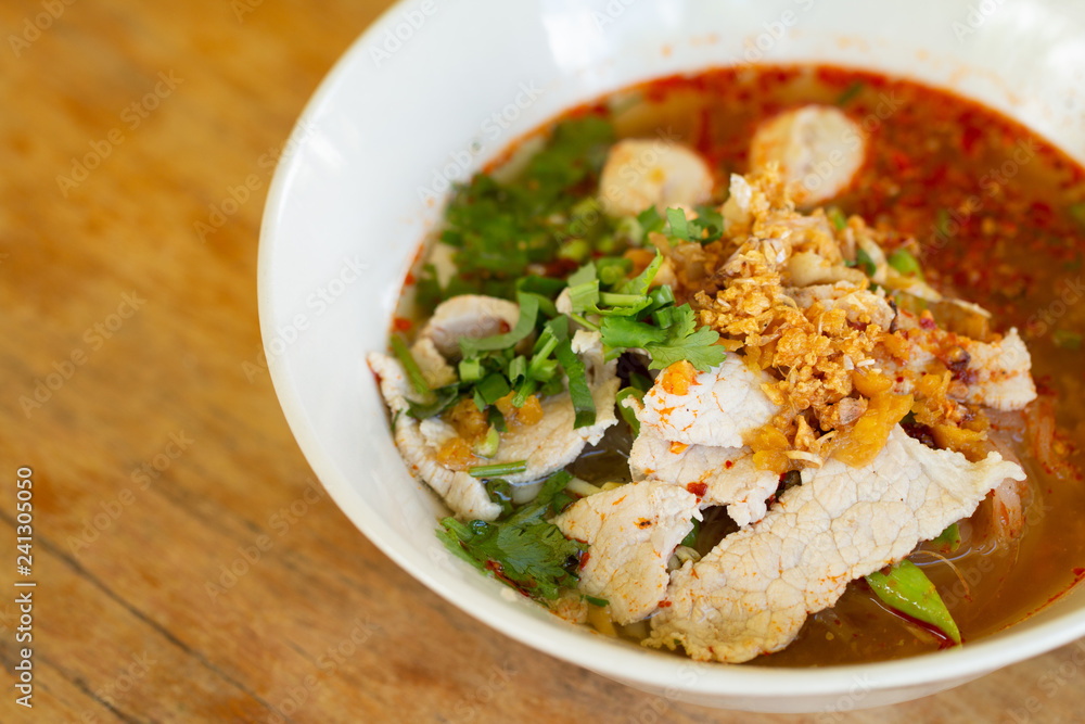 Rice noodle in spicy soup with pork ball, vegetable and pork serving on wooden desk in canteen