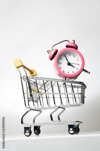 Alarm clock and shopping trolley on a sloping surface. Time to shop.