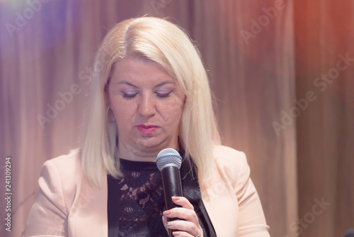 Beautiful business blonde woman with microphone in her hand speaking at the conference or seminar.
