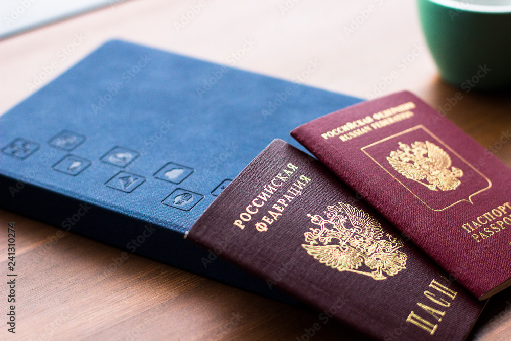 Travel, working, holiday, business concept. Russian passports lie on the background of a notebook, a Cup and a wooden table, сloseup photo. Travel, working, holiday, business concept. Russian passports lie on the background of a notebook, a Cup and a wooden table, сloseup photo.