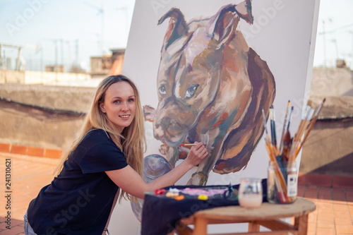 Young woman paint artist drawing at home roof. Picture of bulldog on big canvas. Outdoors art